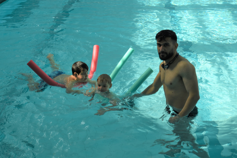 Kinder mit Schwimmnudel und Trainer